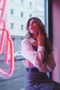 A fashionable woman posing by a vibrant neon window in Berlin.