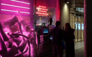 Street scene in Osaka with a neon-lit storefront displaying mannequins and two people observing.